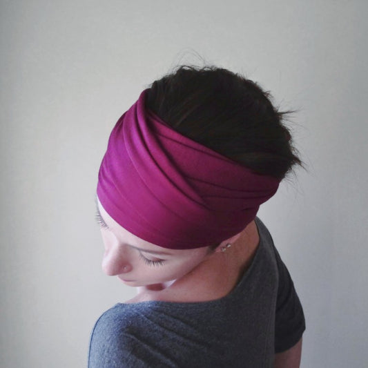 A woman wearing a vibrant magenta head scarf with her hair tied back